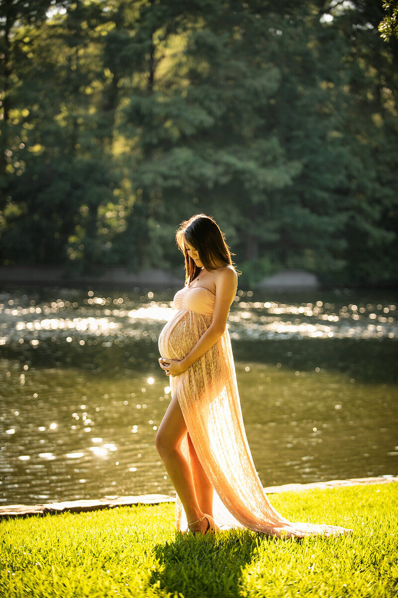A pregnant woman in a flowing gown at golden hour by the water in Dallas