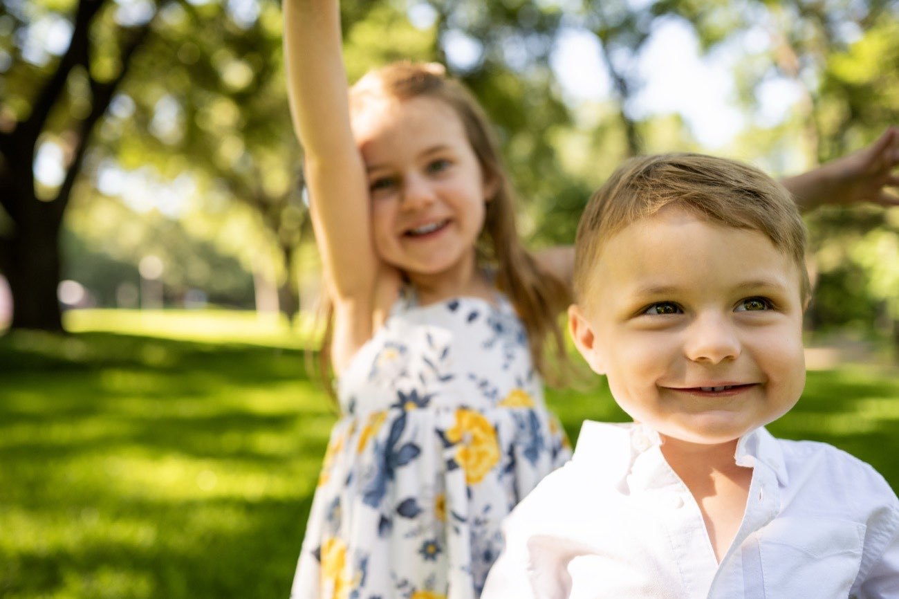 Two children running and laughing through a Dallas park during a family session