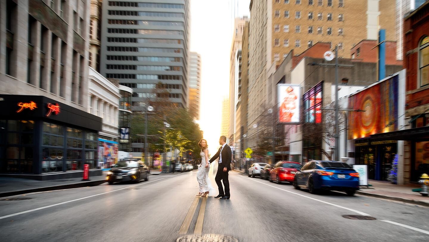 Wide shot of a bride and groom standing in the middle of Main Street in downtown Dallas at sunset.