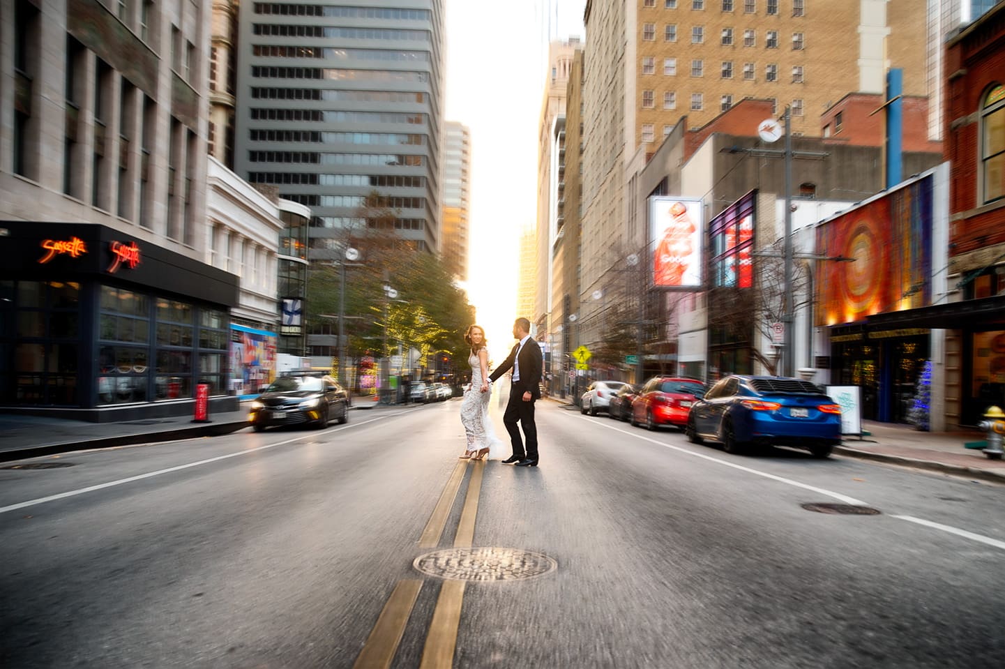 Wide shot of a bride and groom standing in the middle of Main Street in downtown Dallas at sunset.