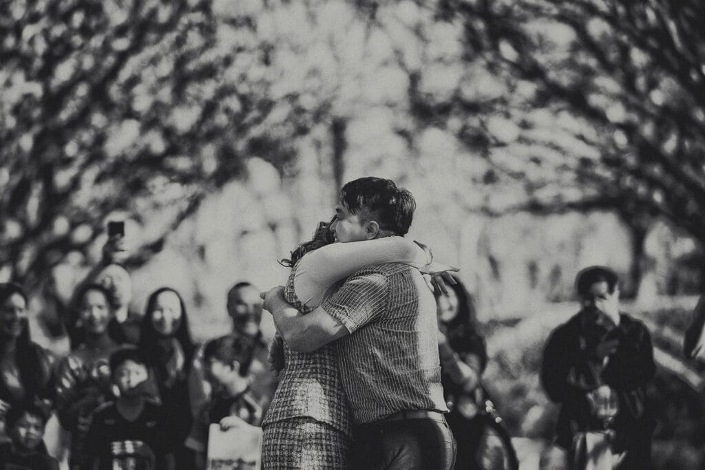 Black and white photograph of a newly engaged couple hugging tightly immediately after a surprise proposal at the Dallas Arboretum.
