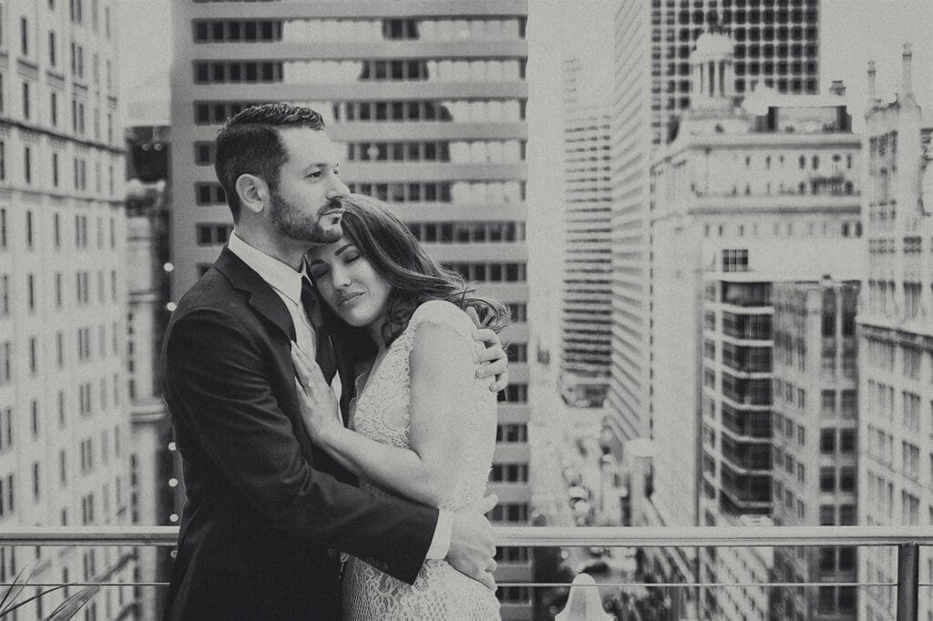 Black and white portrait of a bride resting her head on the groom's chest overlooking the downtown Dallas skyline.