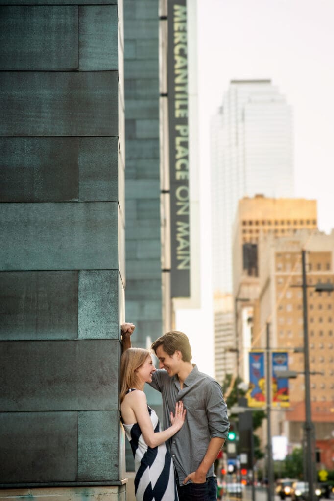 Couple sharing an intimate moment against the copper facade of Mercantile Place on Main with the Dallas skyline in the background
