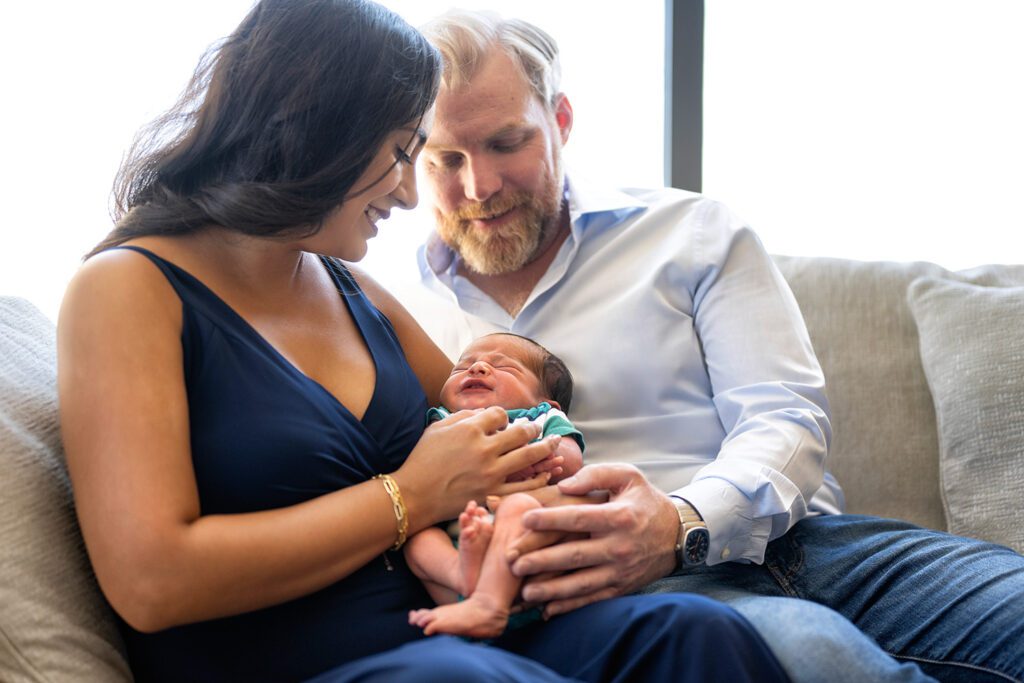 Natural light lifestyle newborn photography of a mother and father smiling down at their baby during a Dallas in-home session.