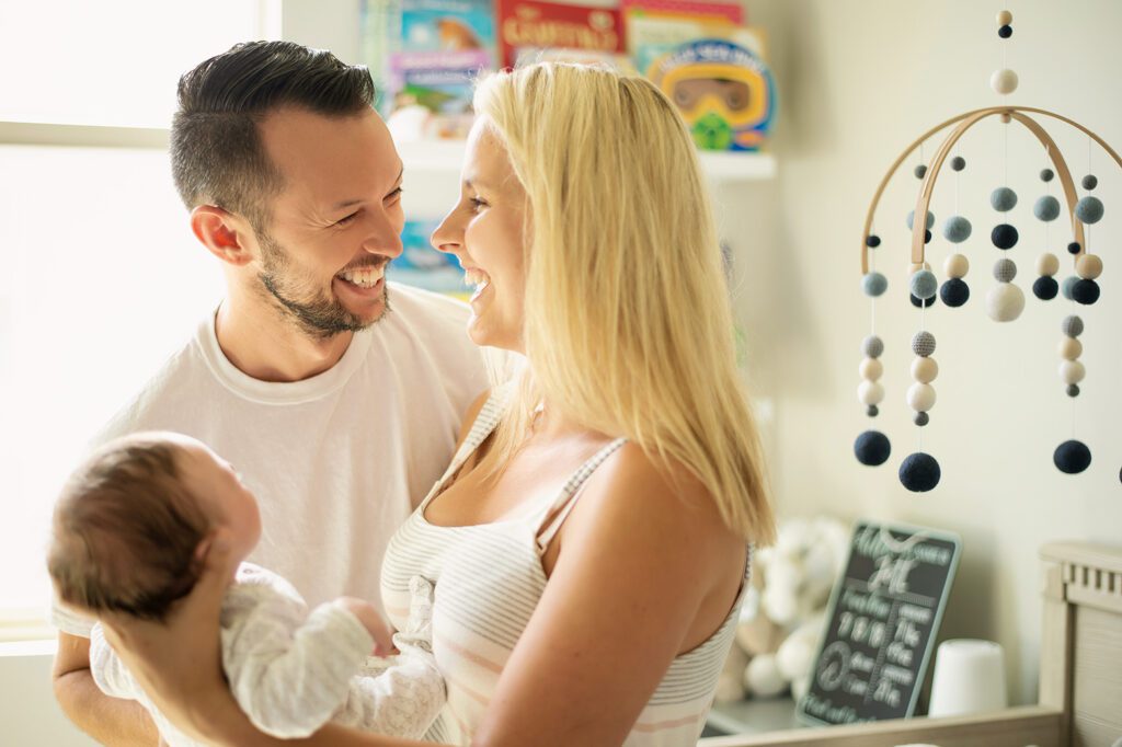 Dallas lifestyle newborn photographer captures candid moment of mom and dad holding their baby in a styled nursery.