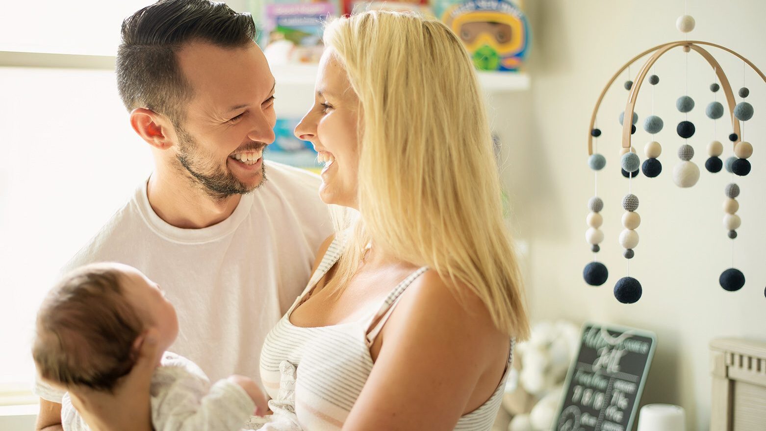 Dallas lifestyle newborn photographer captures candid moment of mom and dad holding their baby in a styled nursery.