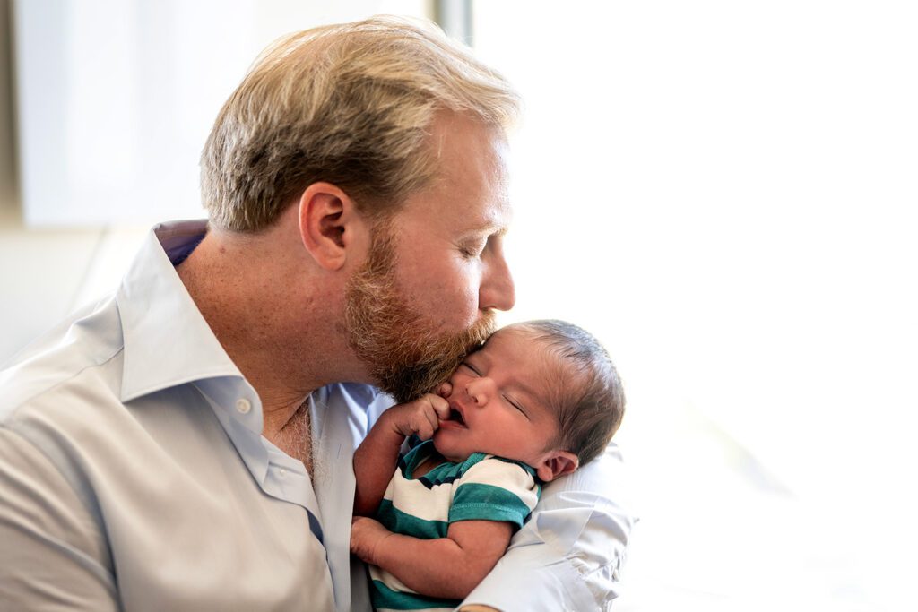 Highland park newborn photographer captures an intimate lifestyle moment of a father kissing his new baby's forehead.