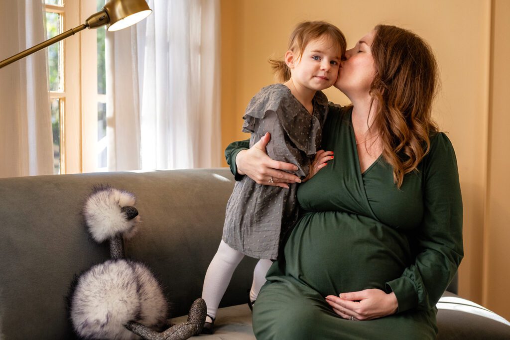 Mom to be kissing toddler in Dallas living room.