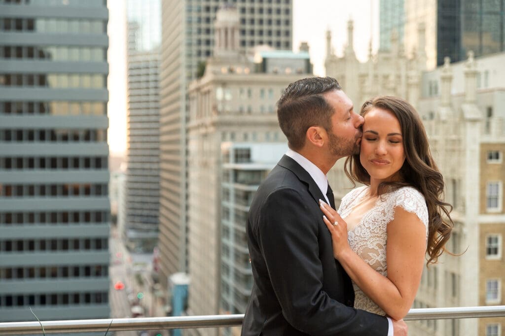 Groom kissing bride on the cheek on the glass rooftop terrace of The Joule in downtown Dallas.